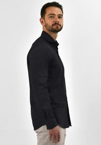 Zwarte langemouwenshirt met een button-down kraag, met een gladde textuur en een rechte snit, gedragen met lichtgekleurde broek.