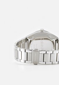 Reloj de acero inoxidable plateado con un acabado pulido y cepillado, que presenta una caja redonda lisa y una pulsera de eslabones. Nombre de la marca grabado visible.