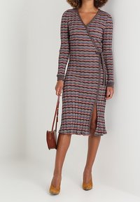 Robe à rayures de style portefeuille avec manches longues, présentant un col en V et une fente latérale. Le matériau est côtelé avec un mélange de couleurs en motif ondulé.