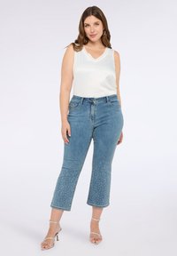 Letvægts cremefarvet top uden ærmer parret med mid-rise blå jeans med udsmykkede nitter ved kanten og sølvfarvede strop sandaler.