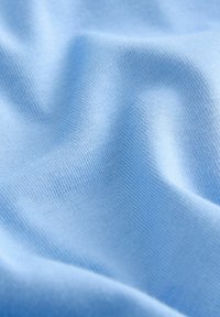Svetlomodro blago z gladko teksturo, s finim pletenim vzorcem in subtilnim sijajem, razpeto, da pokaže svoje mehke, tekoče lastnosti.