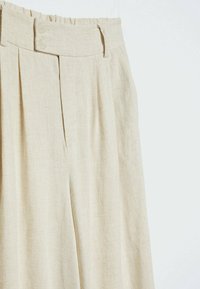 Beige linnen broek met een hoge taille, voorzien van twee knopen en voorplooien. De stof heeft een gestructureerde weving en een zachte afwerking.