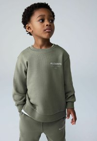 Oliivinvihreä collegepaita, jossa on resorit hihansuissa ja helmassa, valkoinen logo rinnassa. Yhdistetty samaan sarjaan kuuluviin housuihin, pehmeä tekstuuri.