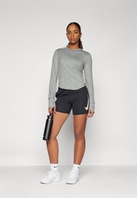 Grå langærmet skjorte med rund hals, parret med sorte atletikshorts med et hvidt logo. Sort vandflaske og hvide sneakers.