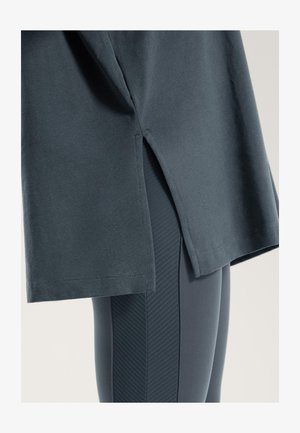 T-shirt in cotone grigio scuro con spacchi laterali, abbinato a leggings grigio scuro con un motivo a strisce verticali testurizzate.