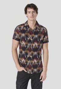 Košeľa s krátkym rukávom a zapínaním na gombíky v tmavej látke s viacfarebným abstraktným vzorom obsahujúcim červené, žlté a biele akcenty.