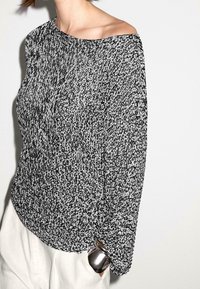 Black and white knitted sweater with an asymmetrical neckline, loose fit, and textured fabric. Silver hardware detail on the side.
