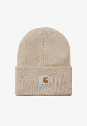 Gorro de punto color marrón claro con un dobladillo, que presenta un parche de logo cuadrado en gris y naranja. Fabricado con un material suave y texturizado.