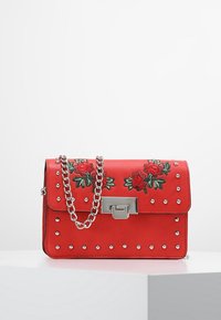 Borsa a tracolla in pelle rossa con ricami floreali, borchie argentate e tracolla a catena. Presenta una forma rettangolare e chiusura con gancio metallico.