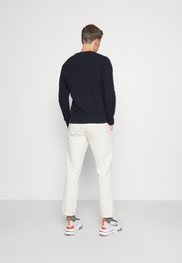 Navy strikkegenser, beige bukser, hvite sneakers med oransje detaljer. Avslappet passform, rund hals, strukturert stoff, synlig design på ryggen.