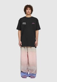 Melna pārmēra t-kreklu ar baltu drukājumus „& Retro Future” un rozā logo; apvienots ar pasteļtoņu gradienta platām biksēm un purpura apaviem.