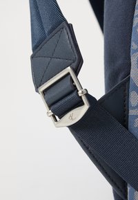 Sangle en tissu bleu marine avec une boucle en métal argenté rectangulaire, présentant un accent en cuir et une couture texturée pour le renforcement.
