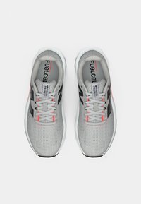 Baskets de sport gris clair avec une tige en mesh texturé, accents noirs, détails réfléchissants et lacets orange ; semelle en caoutchouc au design incurvé.