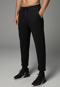 Zwarte textuur joggingshorts met een elastische tailleband en trekkoord, voorzien van zijzakken. Gecombineerd met zwarte sportschoenen.