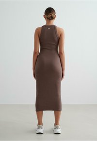 Brown ribbed midi dress with a fitted silhouette, sleeveless design, and a straight hem. Worn with white sporty sneakers.