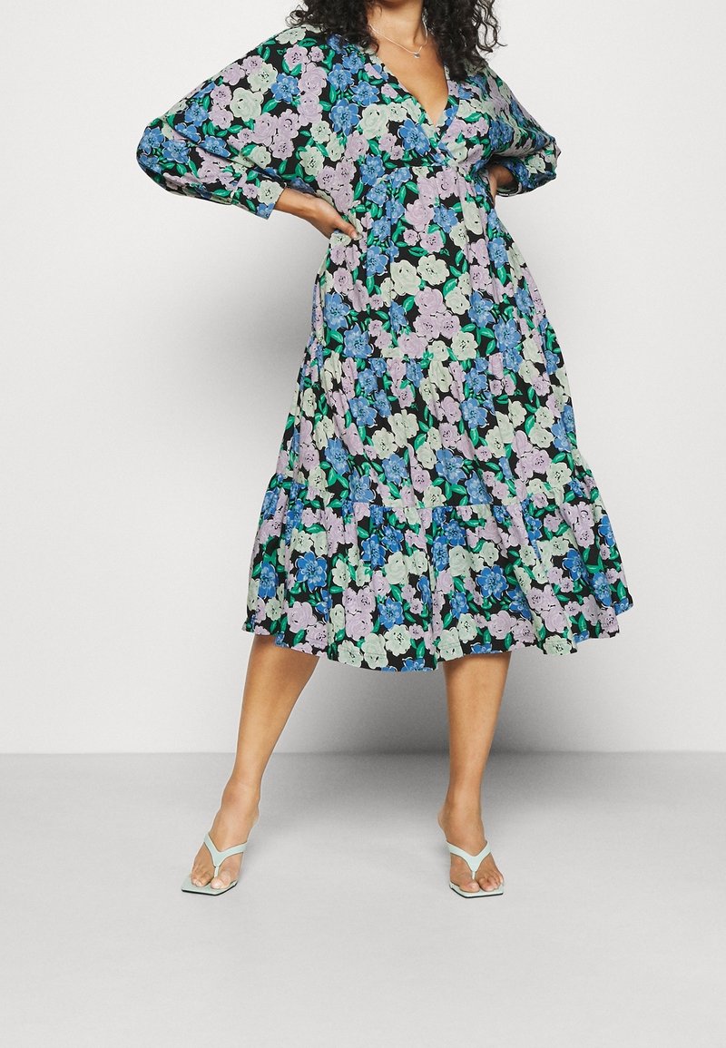 Blommig maxiklänning i svart, med stora blå, lavendel- och gröna blommor, V-ringning, vida ärmar och flerlagrat volangslut.