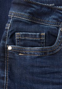 Jeans en denim bleu foncé avec une petite poche avant. Caractéristiques de coutures contrastantes et d'un bouton en métal. La texture est lisse avec un léger décoloration.