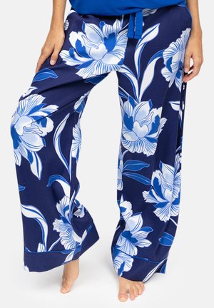 Pantaloni blu navy a vestibilità rilassata con grandi motivi floreali bianchi e blu, indossati a piedi nudi, visibili dalla vita ai piedi.