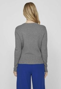 Suéter gris de canalé con cuello redondo, mangas largas y silueta ajustada, combinado con pantalones de pierna ancha azules. Diseño simple y texturizado.