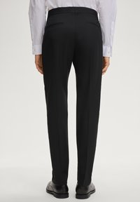 Schwarze, maßgeschneiderte Hose mit glatter Textur, gerade geschnitten, mit zwei Gesäßtaschen, kombiniert mit schwarzen Anzugschuhen.