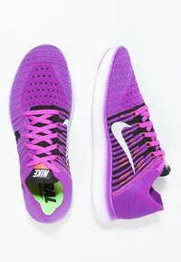 Zapatillas deportivas moradas con parte superior de punto que cuenta con acentos en negro y un logo Swoosh blanco. La suela exterior es blanca con un tono púrpura translúcido.