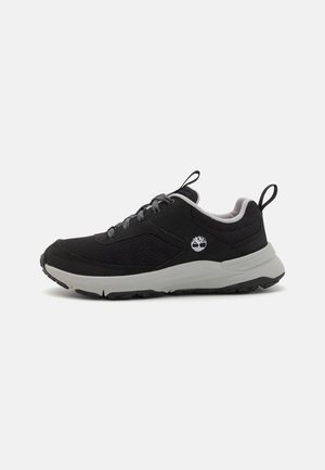 Sorte joggesko med et mesh- og syntetisk overdel, grå detaljer, og en polstret grå såle. Har flate lisser og en logo på siden.