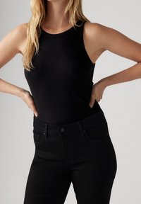 Top sin mangas de color negro con cuello redondo, combinado con jeans ajustados negros. La tela es suave y cuenta con un diseño ceñido.