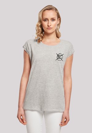 Graues Baumwoll-T-Shirt mit rundem Halsausschnitt und gerollten Ärmeln. Mit einem schwarzen Grafikdruck auf der Brust. Kombiniert mit weißen Hosen.