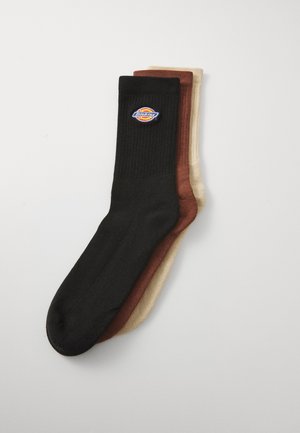 Tres pares de calcetines de tripulación en negro, marrón y beige. El calcetín negro presenta una textura acanalada y un logotipo colorido en el puño.
