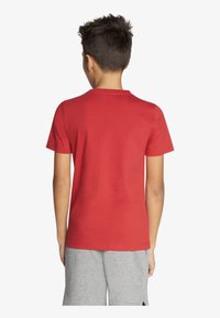 Czerwona bawełniana koszulka z krótkimi rękawami i okrągłym dekoltem, widoczna z tyłu. Prosty wzór, bez widocznych wzorów czy akcentów.