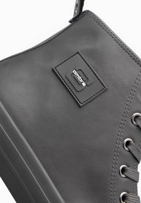 Zapatilla alta negra hecha de cuero sintético con una textura suave, presenta un parche de logo gris, ojales metálicos y cordones a juego.