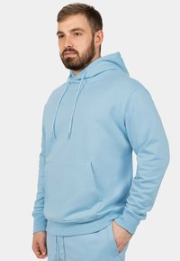 Felpa azzurra chiara in cotone, con tasca frontale, cappuccio con coulisse e polsini a costine. Design semplice con dettagli minimali.