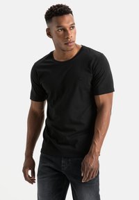 Sort kortærmet t-shirt lavet af bomuld med en rund halsudskæring og et subtilt logo på venstre bryst, parret med mørke jeans.