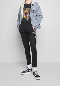 Jeansjacka med shearlingkrage, svart grafisk t-shirt, svarta tapered joggers med vita ränder och svarta sneakers med vita sulor.