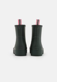 Green rubber ankle boots with a block heel, round toe, and red, white, and black striped pull tabs at the back. Smooth texture, minimalist design.