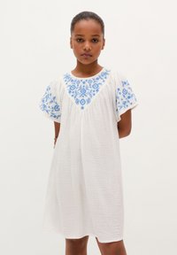 Hvid bomulds kjole med blå broderede blomsterdesign på ærmerne og halsudskæringen. Løs pasform, korte ærmer og struktureret stof.