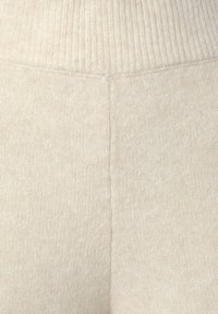 Crème-kleurige gebreide stof met een geribbelde tailleband, met een gladde textuur en subtiele variaties in schaduwwerking.