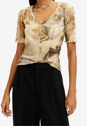 Woman wearing a fitted, beige short-sleeve top with Renaissance-style painting print and black high-waist pants.