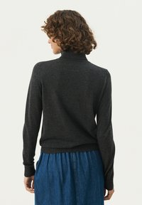 Tmavě šedý svetr s vysokým límcem a dlouhými rukávy, s žebrovanými manžetami a lemem. Nesený přes modrou skládací sukni. Minimalistický design a měkká textura.