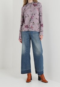 Långärmad lavendelfärgad topp med blommönster och volangkrage, i kombination med vida blå jeans och bruna klackade ankelstövlar.