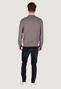 Pull en gris à motifs avec un ourlet côtelé, associé à un jean en denim foncé et des sneakers blanches. Le pull présente un design texturé.