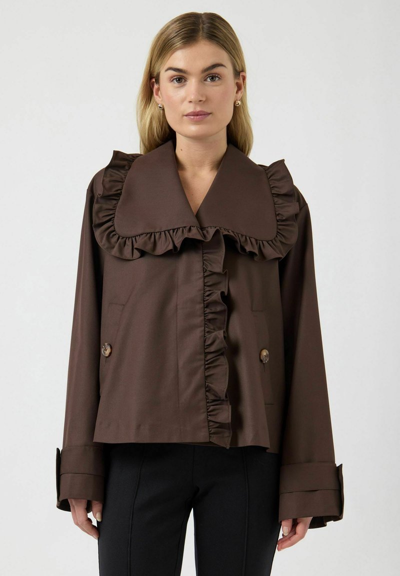 Giacca marrone con volant, ampio colletto, due tasche frontali e dettagli con bottoni. Caratterizzata da un tessuto liscio e una vestibilità comoda.