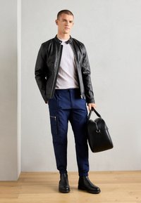 Svart lærjakke, lys grå t-skjorte, marineblå cargo-bukser med glidelåslommer, svarte chelsea-boots og en strukturert svart håndveske.