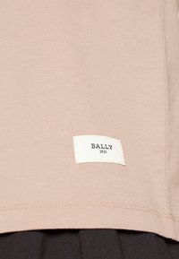 T-shirt Bally en beige clair, fabriqué en coton doux avec une étiquette blanche brodée affichant "BALLY 1851" au bas de l'ourlet.