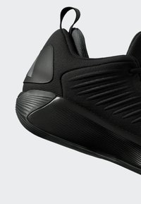 Nahaufnahme eines schwarzen Sportschuhs mit strukturierter Sohle, gepolstertem Absatz, Schlaufe zum Anziehen und atmungsaktivem Obermaterial aus Strick mit gesteppten Details.