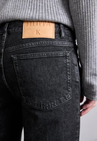 Svart denimjeans med et lærpatch bak som har påskriften "Filippa K," med klassisk femlommers design og en teksturert stoff.