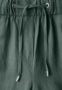 Shorts en tissu vert avec une taille à cordon. Le matériau est léger avec une texture douce. Présente des accents métalliques sur les extrémités du cordon.