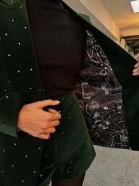 Grön sammetskavaj och shorts prydda med silvernitar; insidan har ett svart mönstrat foder med illustrationer och text.