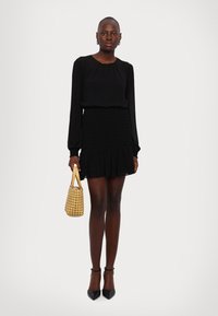 Zwarte blouse met lange mouwen, gecombineerd met een zwarte flare rok; geaccessoreerd met een geweven tan handtas en zwarte pointed heels. Overal een zachte textuur.