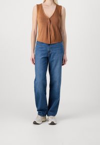 Rdzawoczerwony prążkowany top bez rękawów z głębokim dekoltem w szpic i z przodu guzikami, zestawiony z jasnoniebieskimi dżinsami oraz białymi sneakersami.